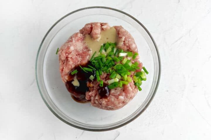 Glass bowl with ground meat, green onions, dark sauce, and light sauce for making subgum wonton soup.