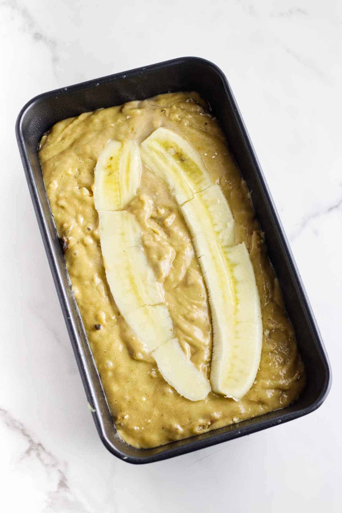 banana bread batter poured into a loaf pan with slices of banana garnishing the top.