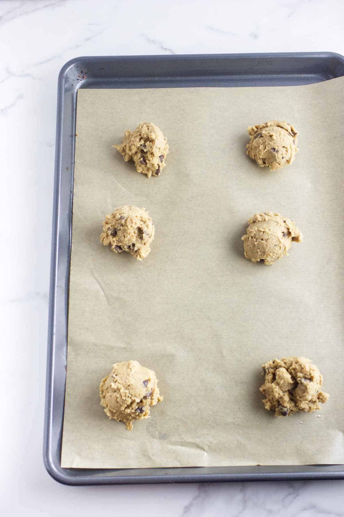 balls of cookie dough on a parchment covered baking sheet.