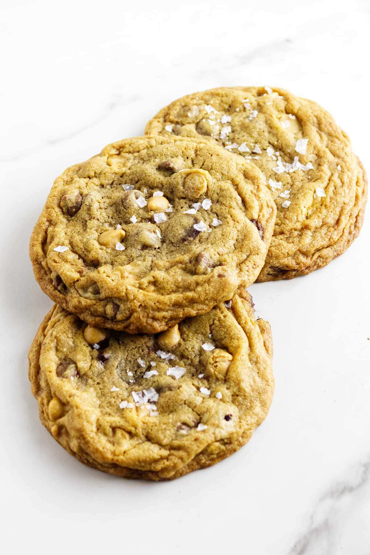 three chocolate chip butterscotch cookies with salt flakes on top.