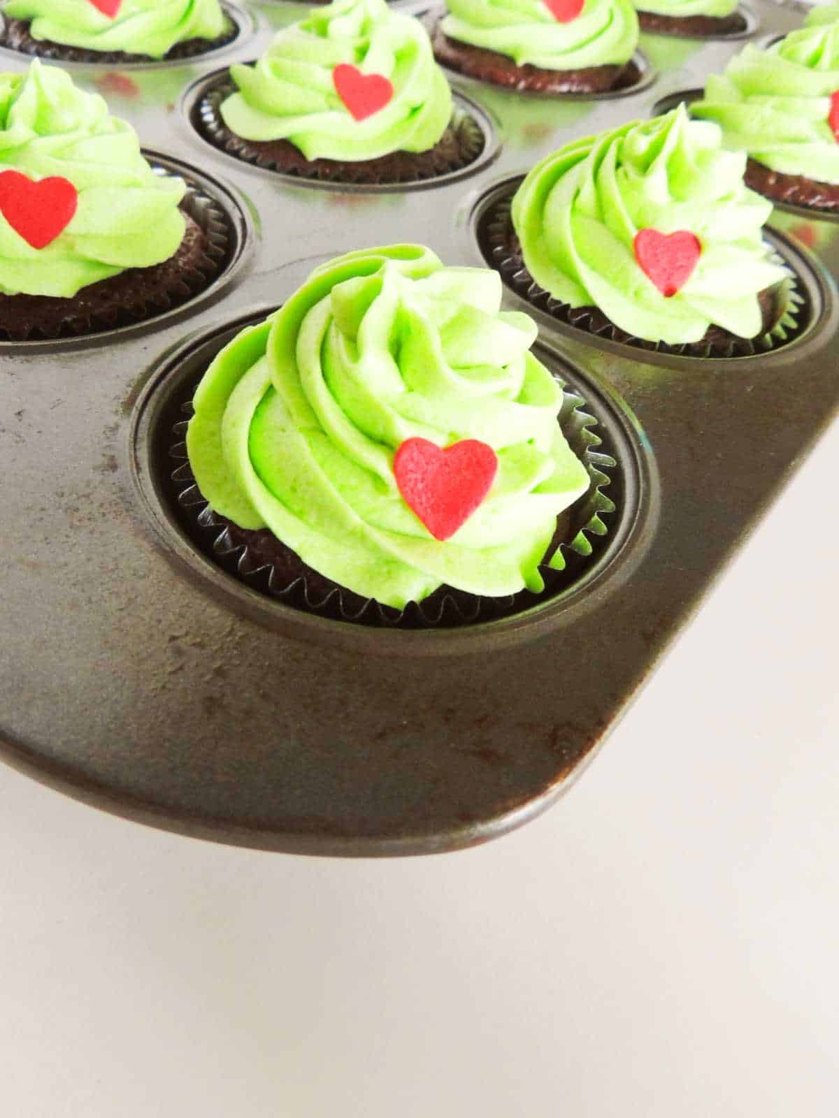 Red candy hearts and green frosting on  cupcakes.