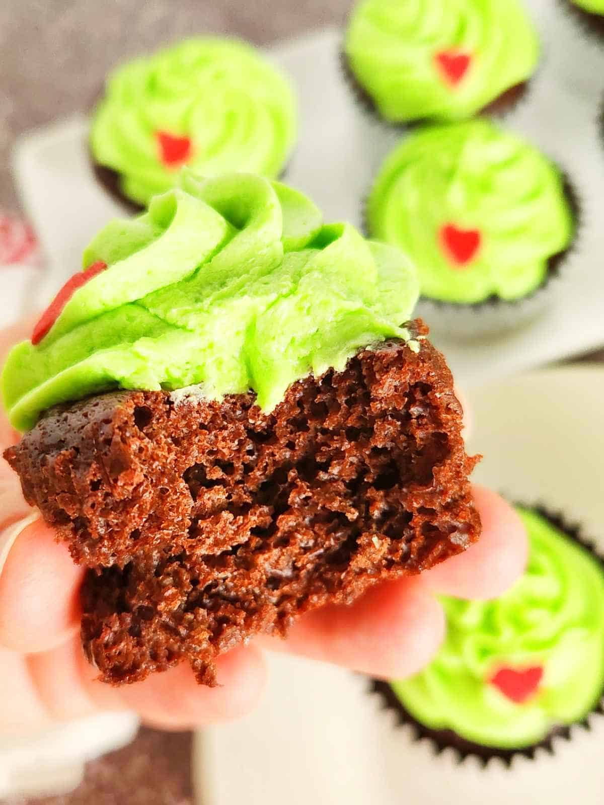 holding unwrapped Grinch cupcake with a bite out of it.