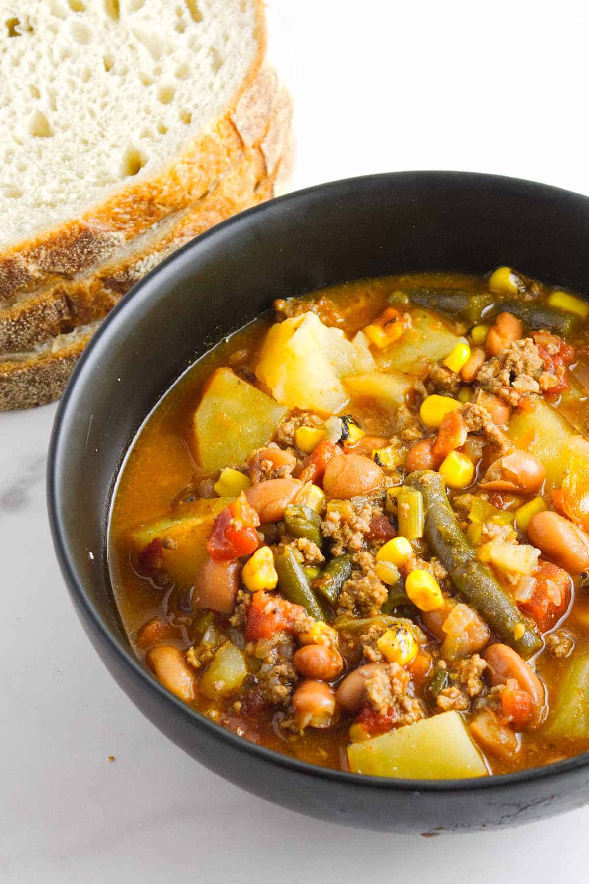 vegetable beef stew in a bowl with bread nearby.