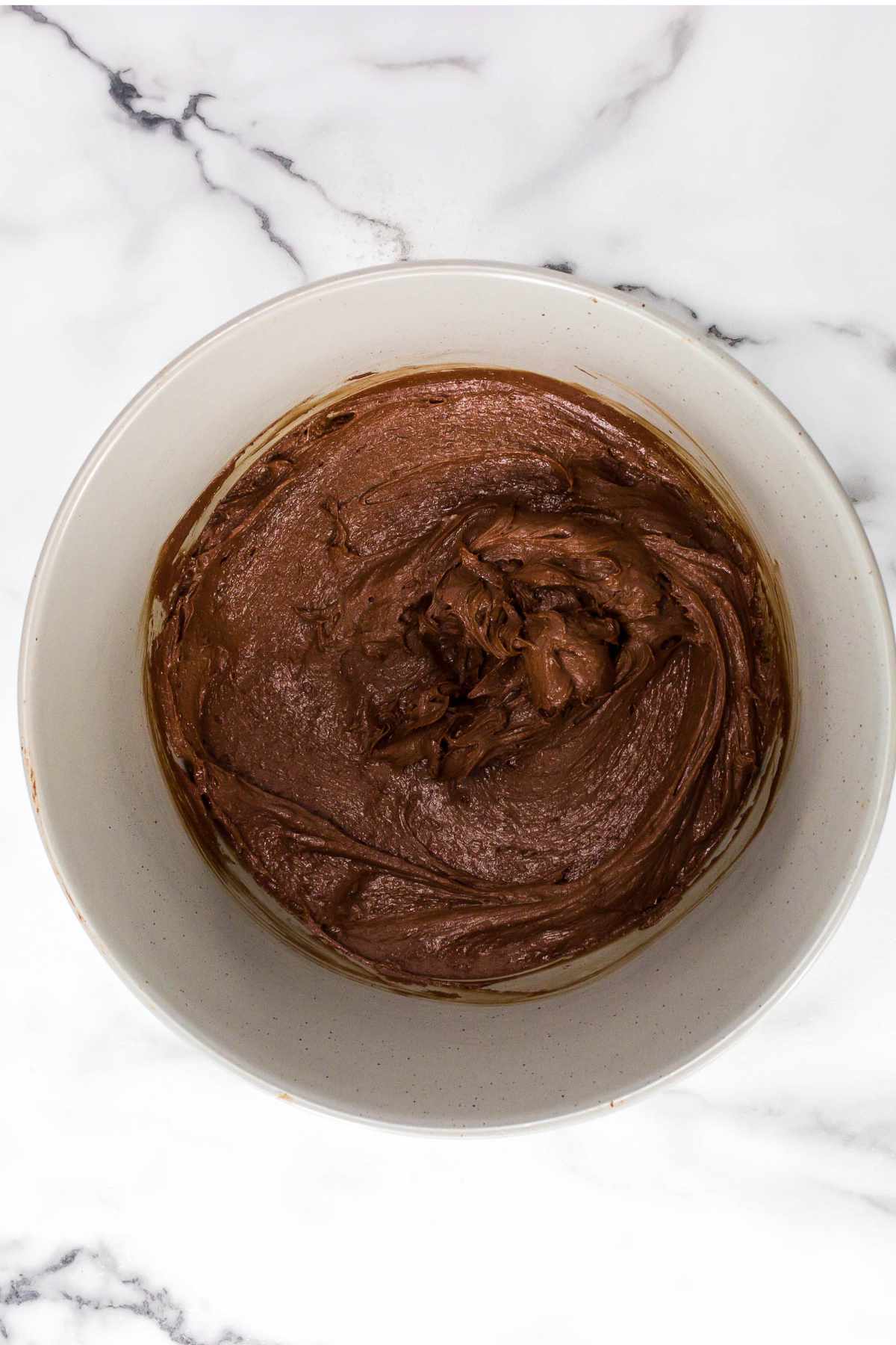 brownie batter in white bowl with beaters nearby.