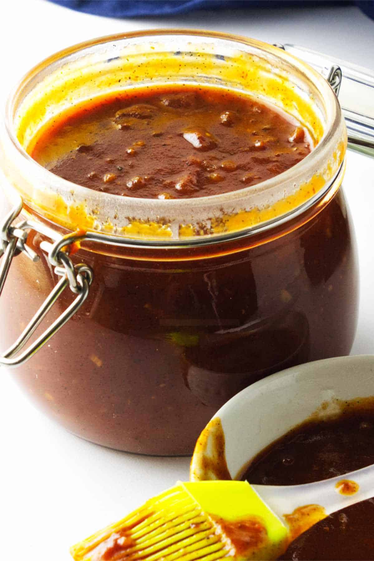 homemade bourbon BBQ sauce in a bail jar with basting brush and bowl of sauce on white background