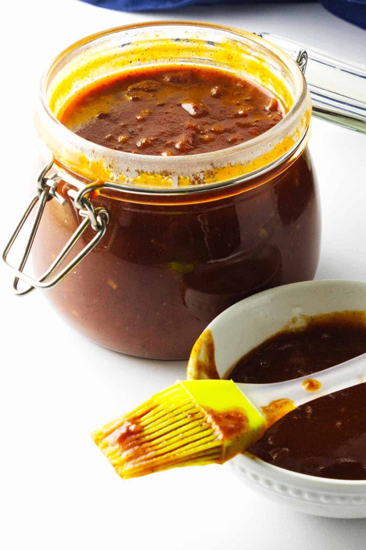 homemade bourbon BBQ sauce in a bail jar with basting brush and bowl of sauce on white background