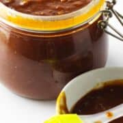 homemade bourbon BBQ sauce in a bail jar with basting brush and bowl of sauce on white background