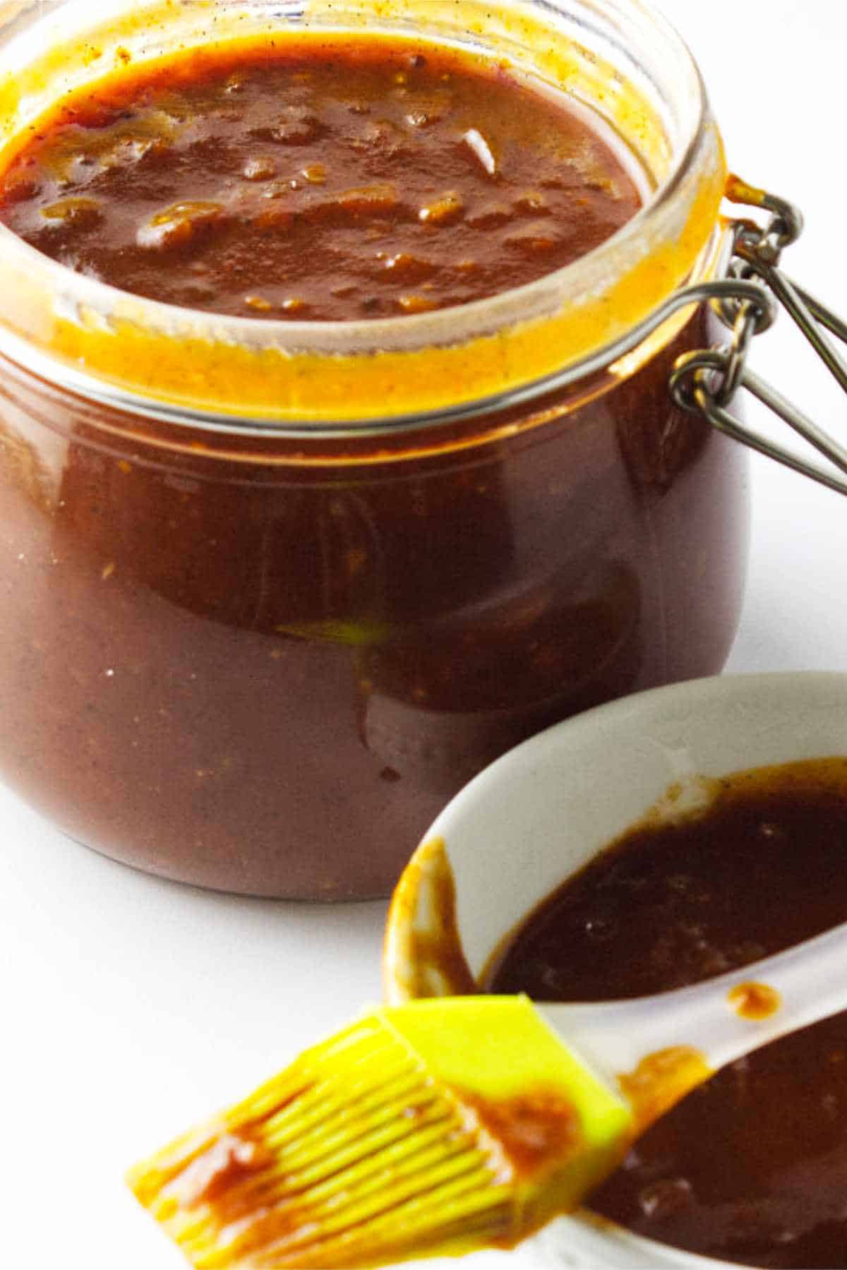 homemade bourbon BBQ sauce in a bail jar with basting brush and bowl of sauce on white background
