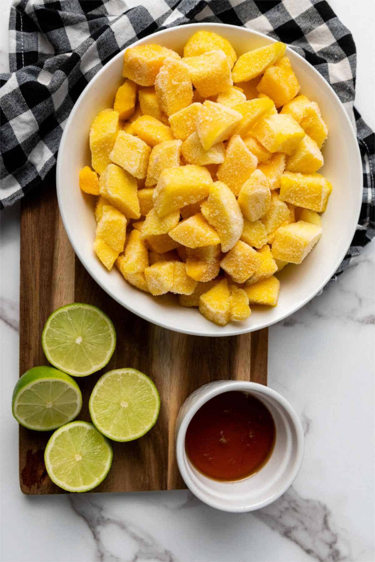 frozen mango chunks in a bowl, honey in a small bowl, and two limes halved.