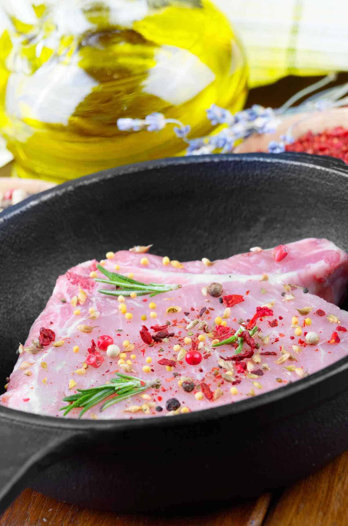 Raw pork rib chops on frying pan with rosemary, pepper garlic and spices.
