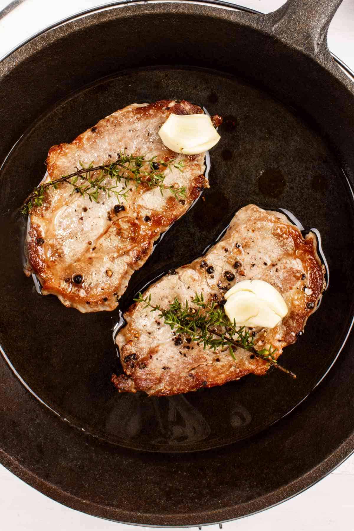 Pan grilled pork chops with thyme and garlic in a cast iron pan.