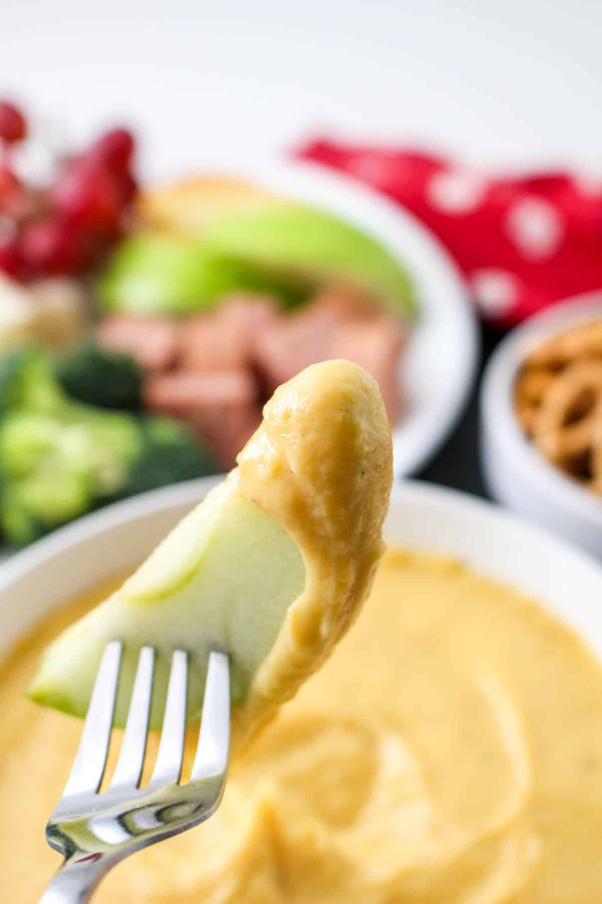 slice of apple on a fork after dipping into cheese sauce.