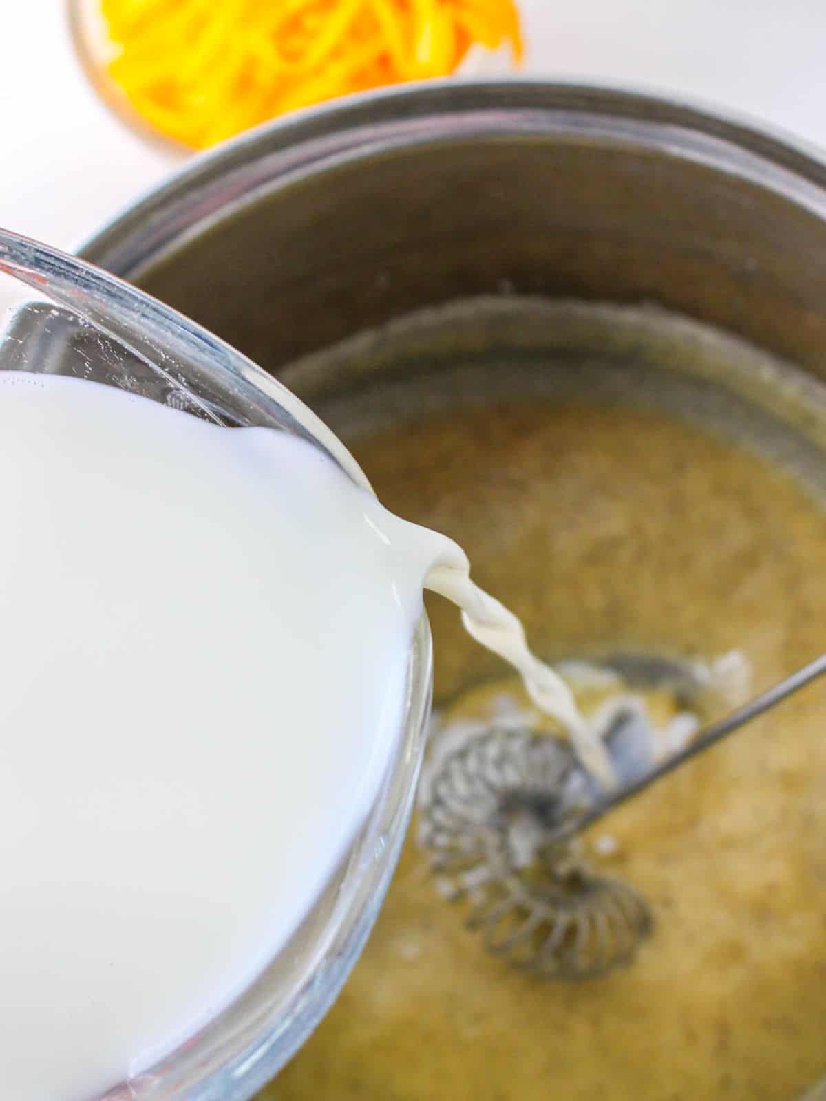 milk slowly pouring and whisked into the pan of roux.