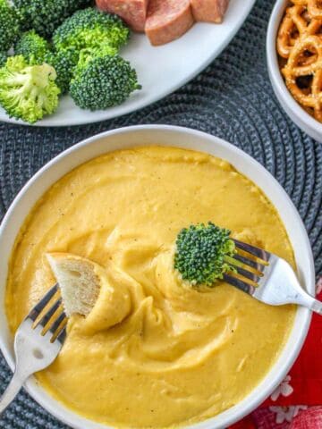 bowl of cheese fondue with bowls of broccoli and pretzels for dipping.