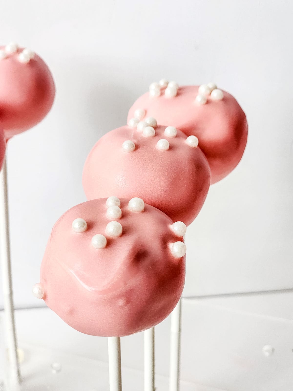 strawberry cake pops with white sprinkles on top.