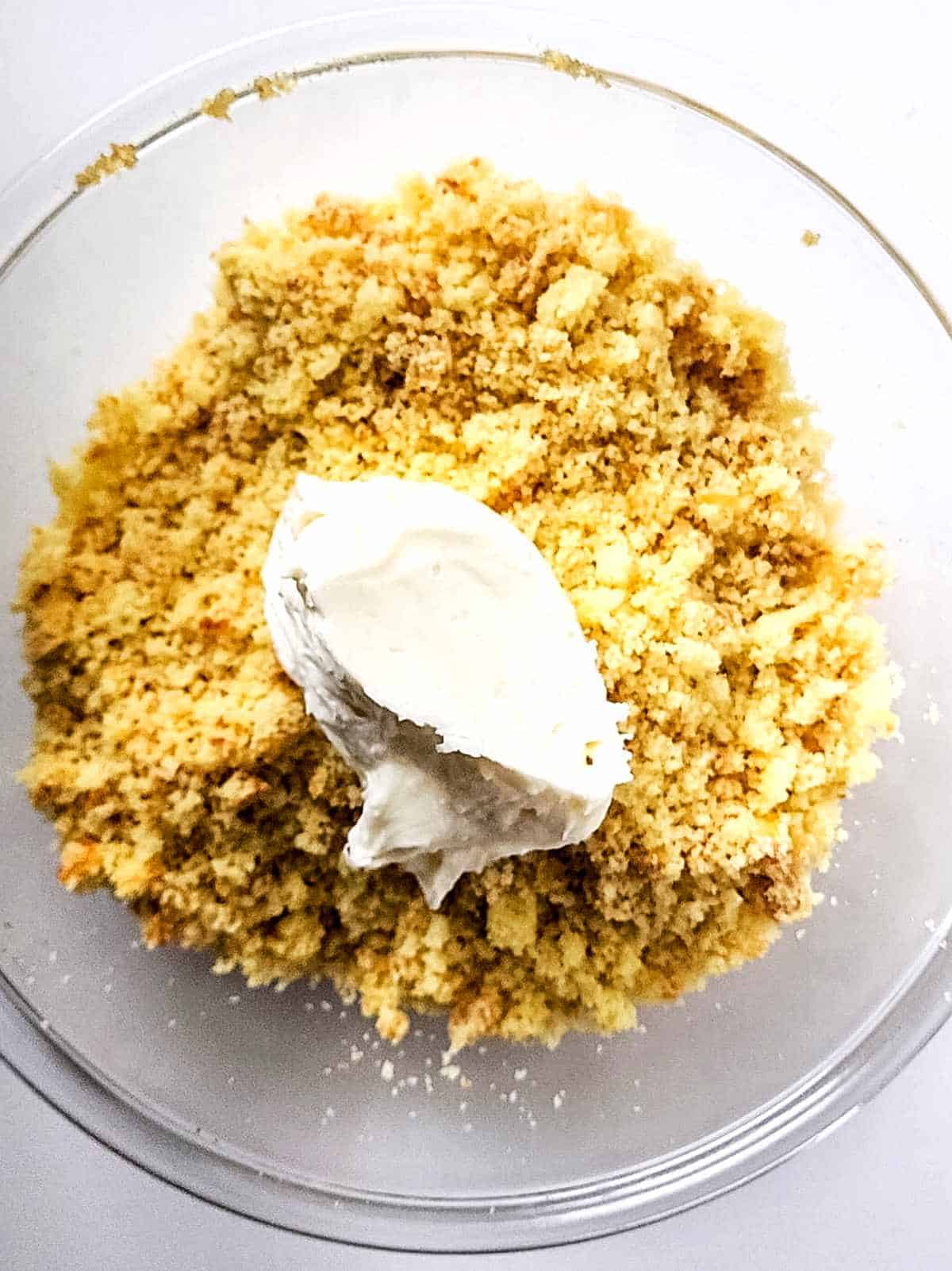 frosting added to bowl of yellow cake crumbles.