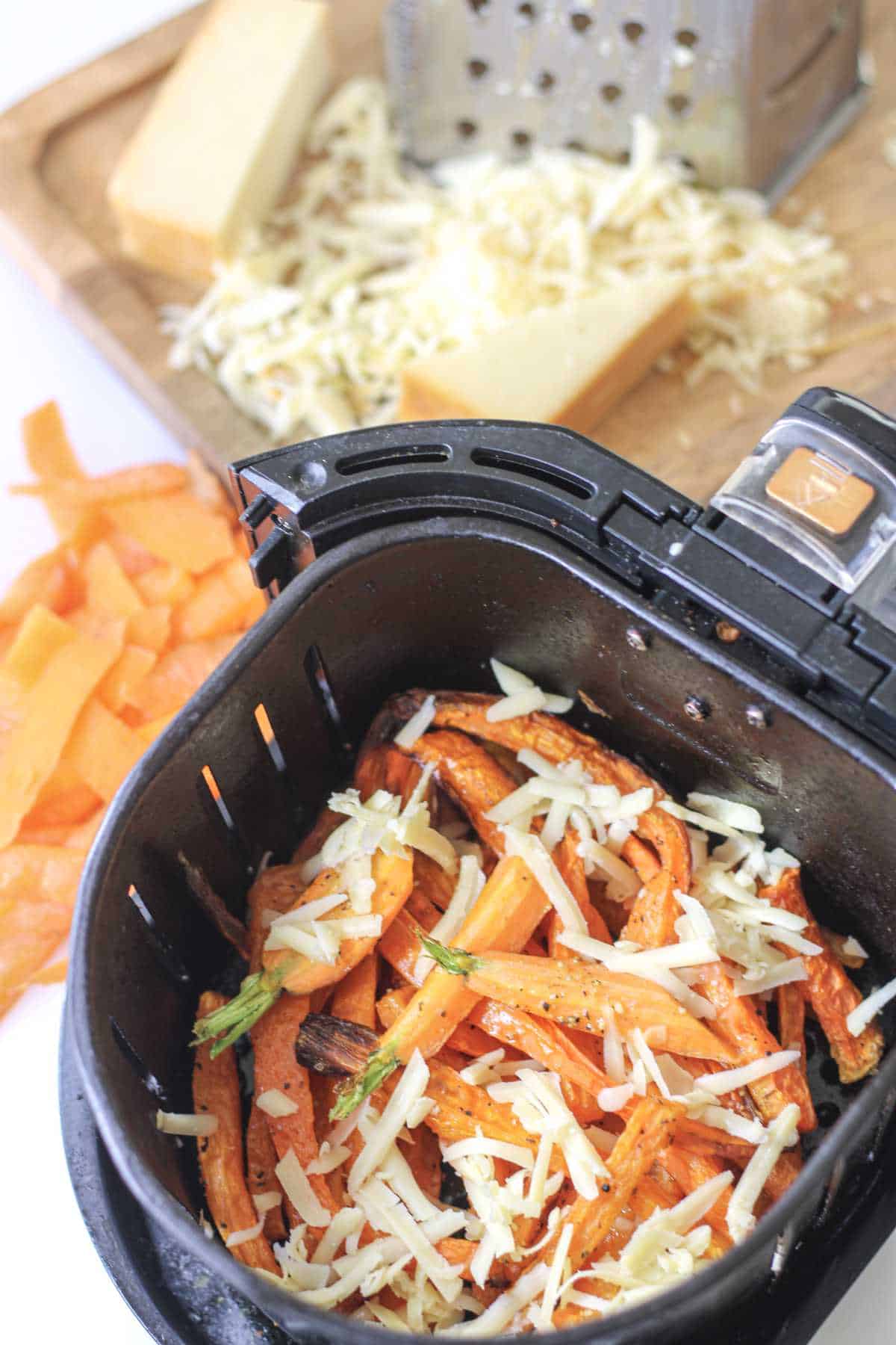 seasoned carrots in an air fryer basket with shredded cheese on top.