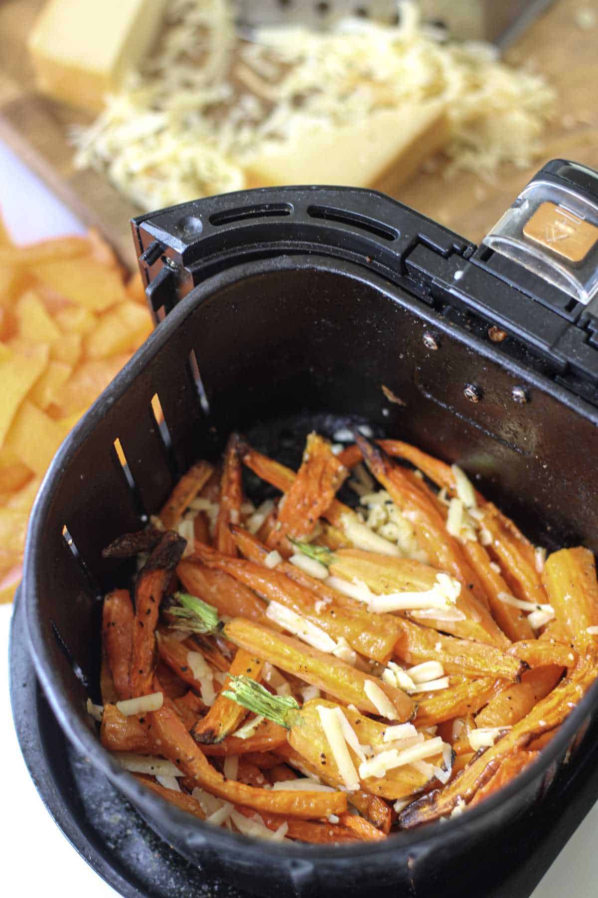 seasoned carrots in an air fryer basket with shredded cheese on top.