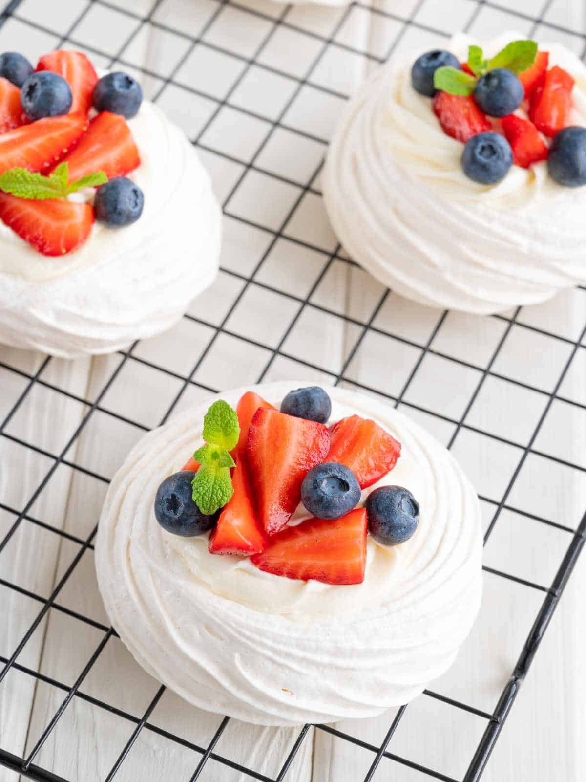 Filled mini pavlova nests with whipped cream and topped with strawberries and blueberries.