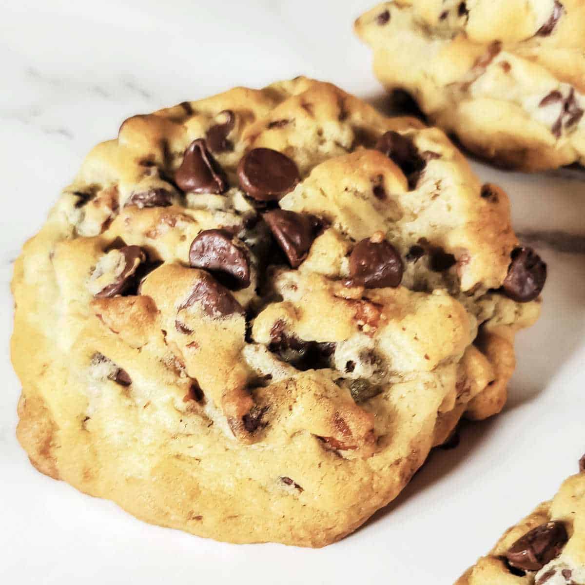 large chocolate chip cookie on a white marble surface.