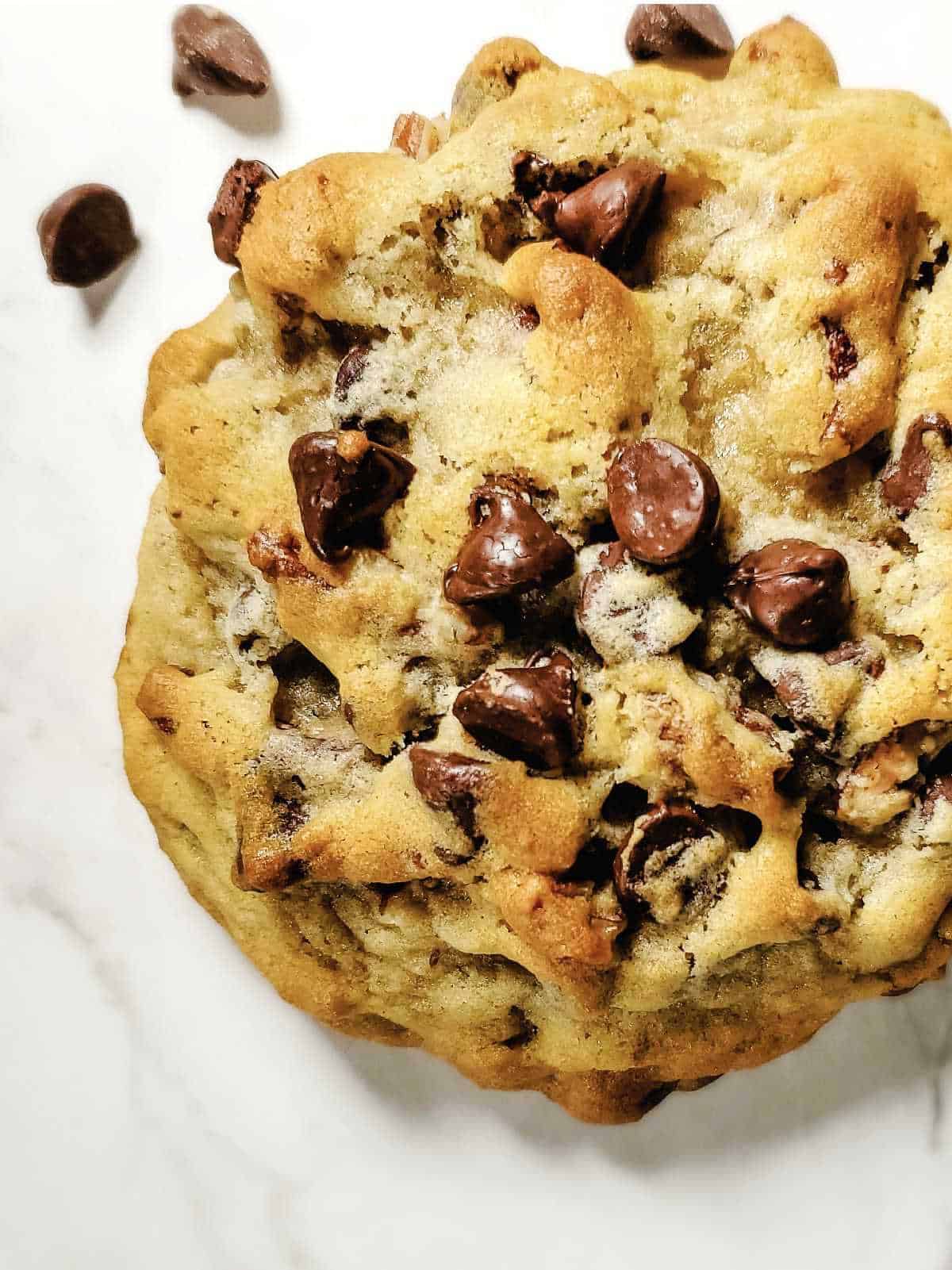 large chocolate chip cookie on a white marble surface.
