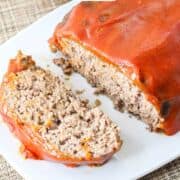 Catsup covered meatloaf on a serving platter with a slice cut.