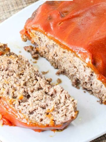 Catsup covered meatloaf on a serving platter with a slice cut.