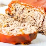 Catsup covered meatloaf on a serving platter with a slice cut.