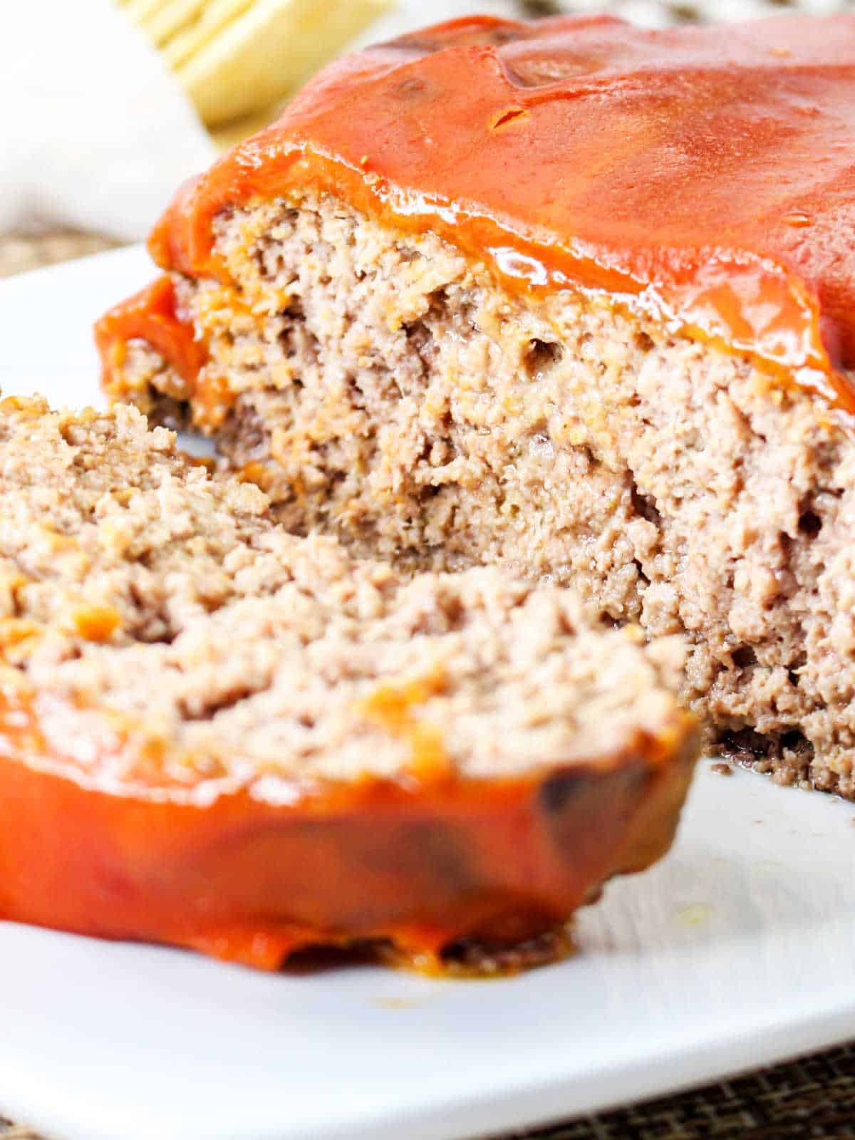 Catsup covered meatloaf on a serving platter with a slice cut.