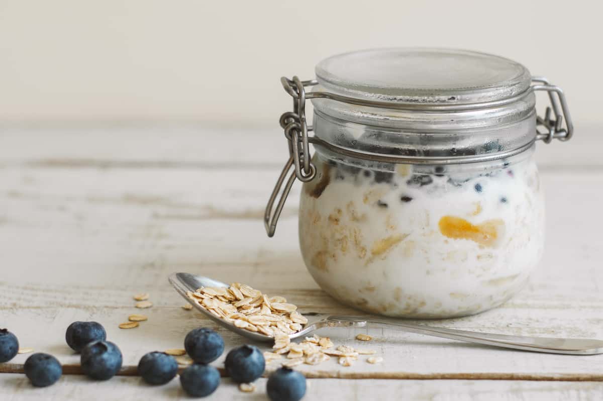 Jar with ready to eat overnight oats with coconut milk and blueberry on wooden table. Breakfast meal.