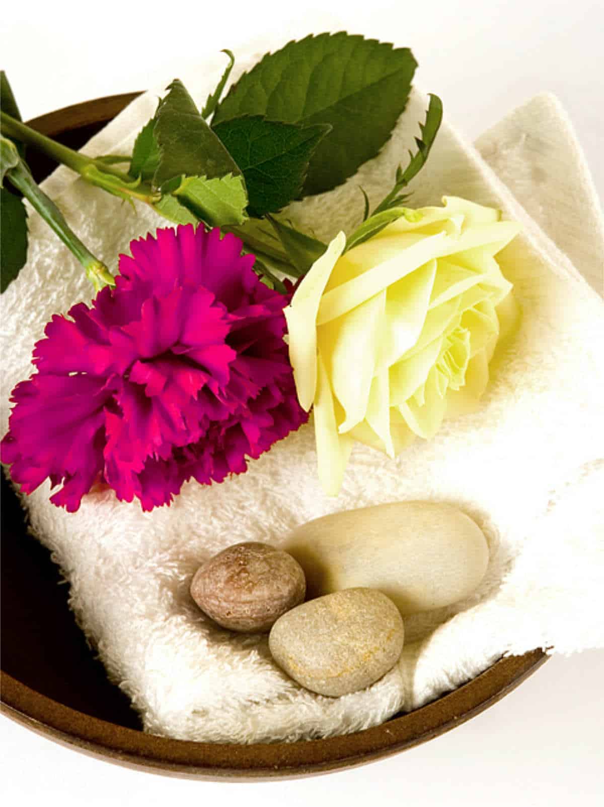 wooden bowl with white towel and scattered pebbles decorated with a white rose and magenta carnation.