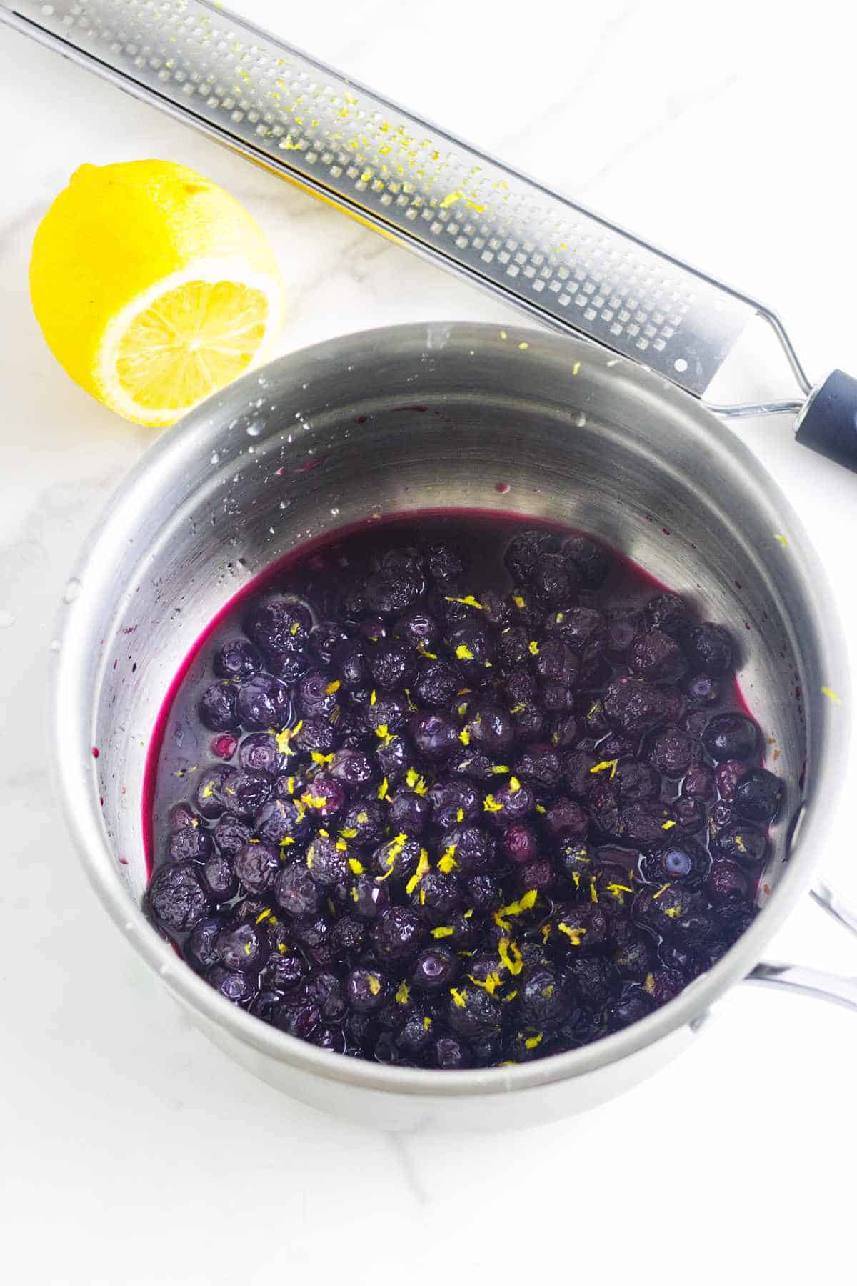 cooked blueberries in a saucepan with fresh lemon zest.