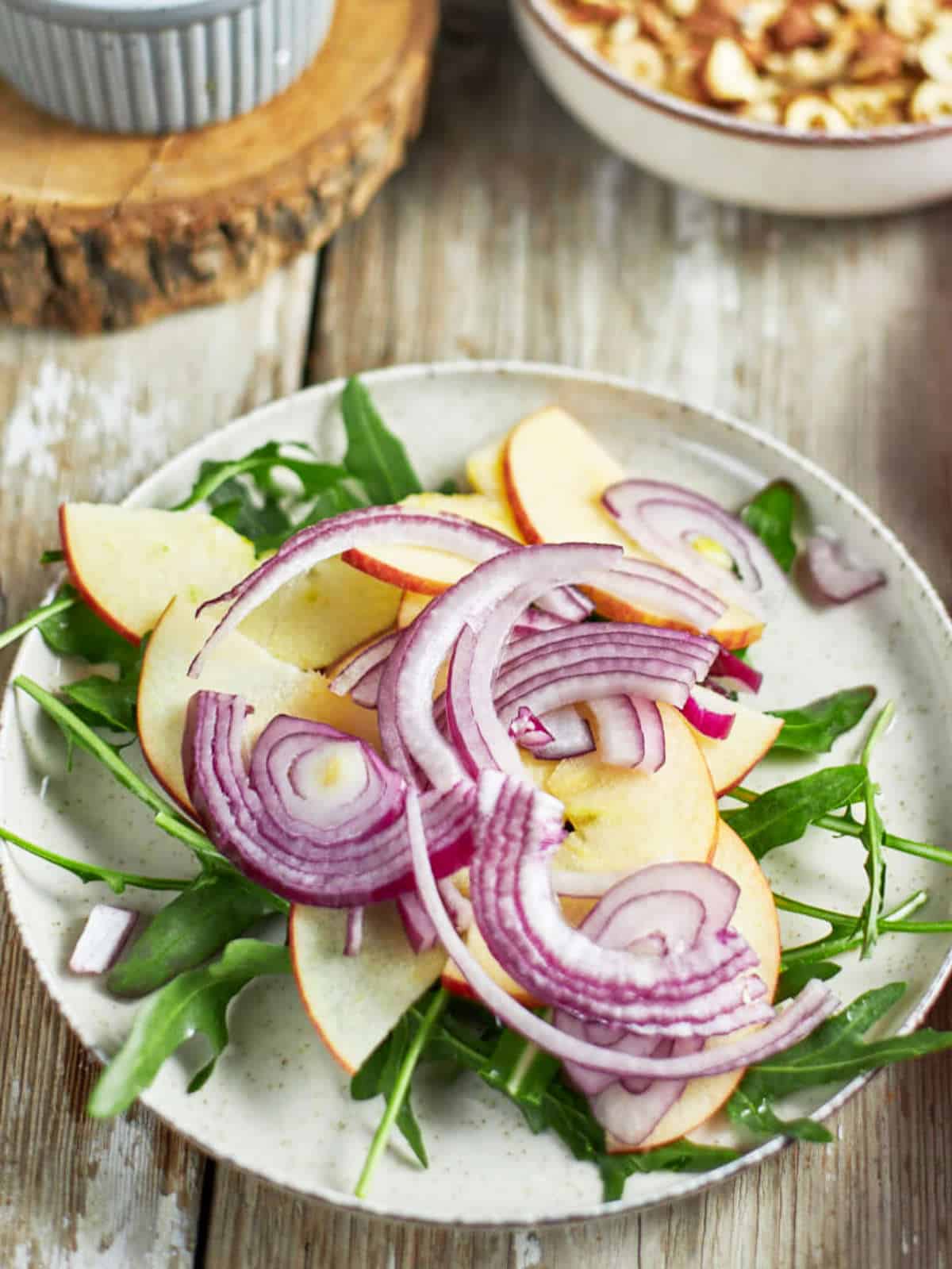 Slices of thin red onion topping slices of apples on arugula.