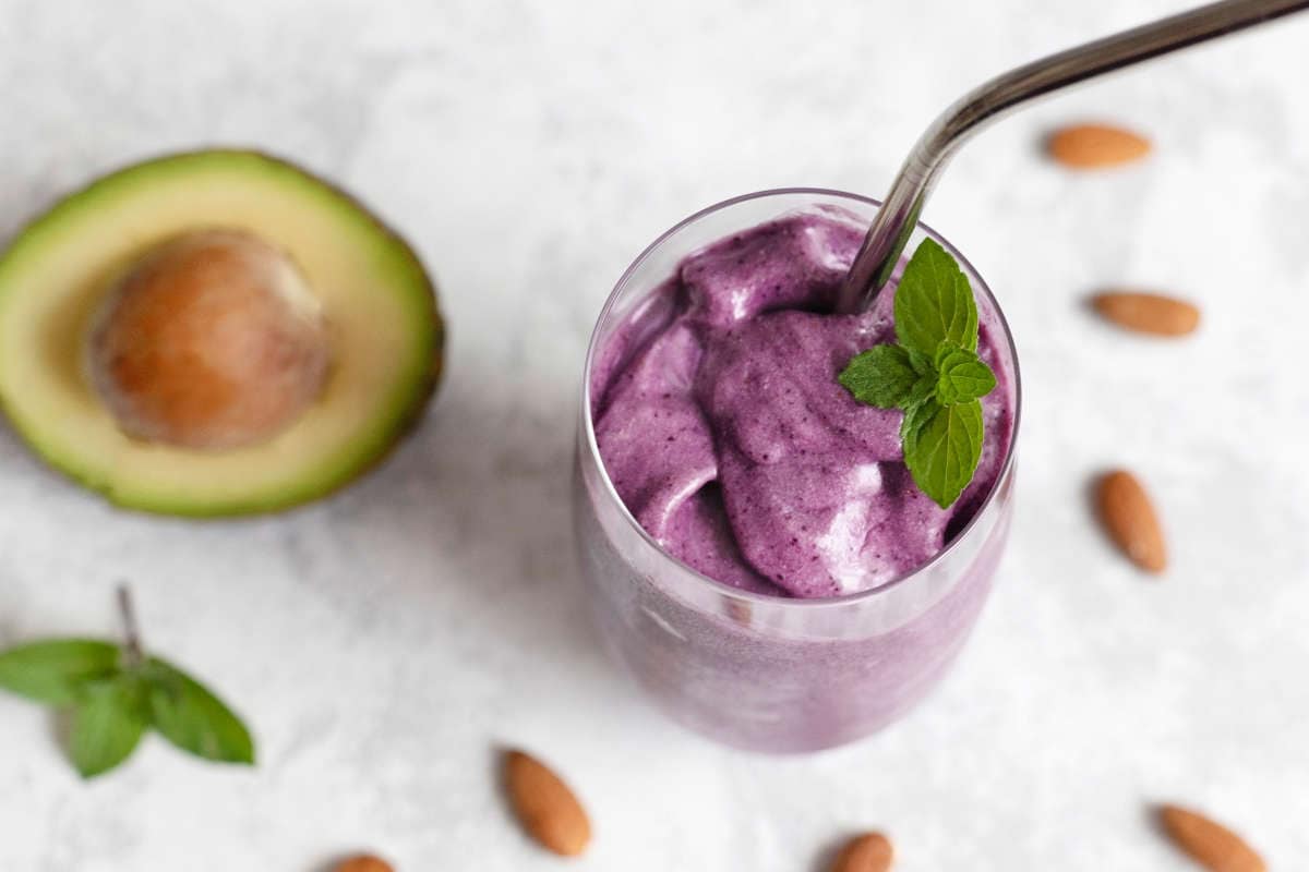 Summer refreshing smoothie with avocado, blueberries and almond milk in a glass glass with a reusable iron straw on a light background. Diet cocktail, keto recipes