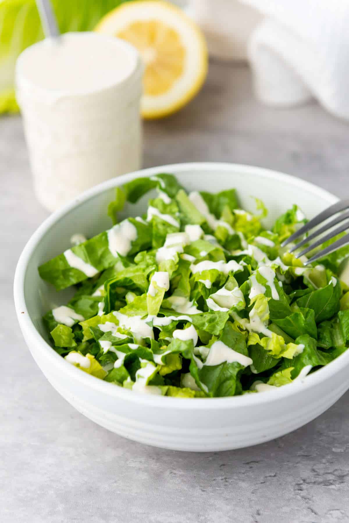 Jar of Caesar salad dressing in the background with a salad drizzled with salad dressing.