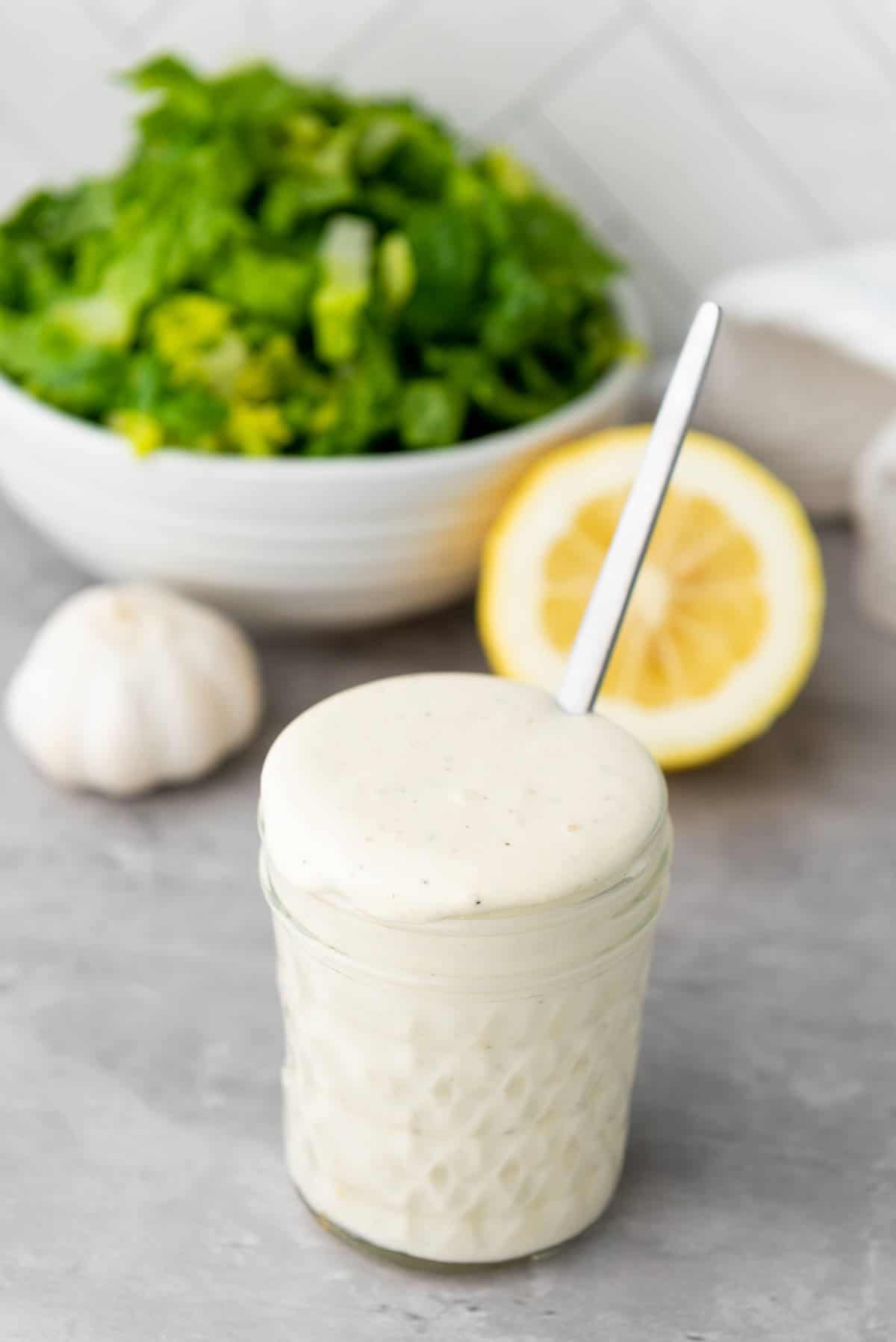 Jar of homemade Caesar salad dressing with a salad in the background.