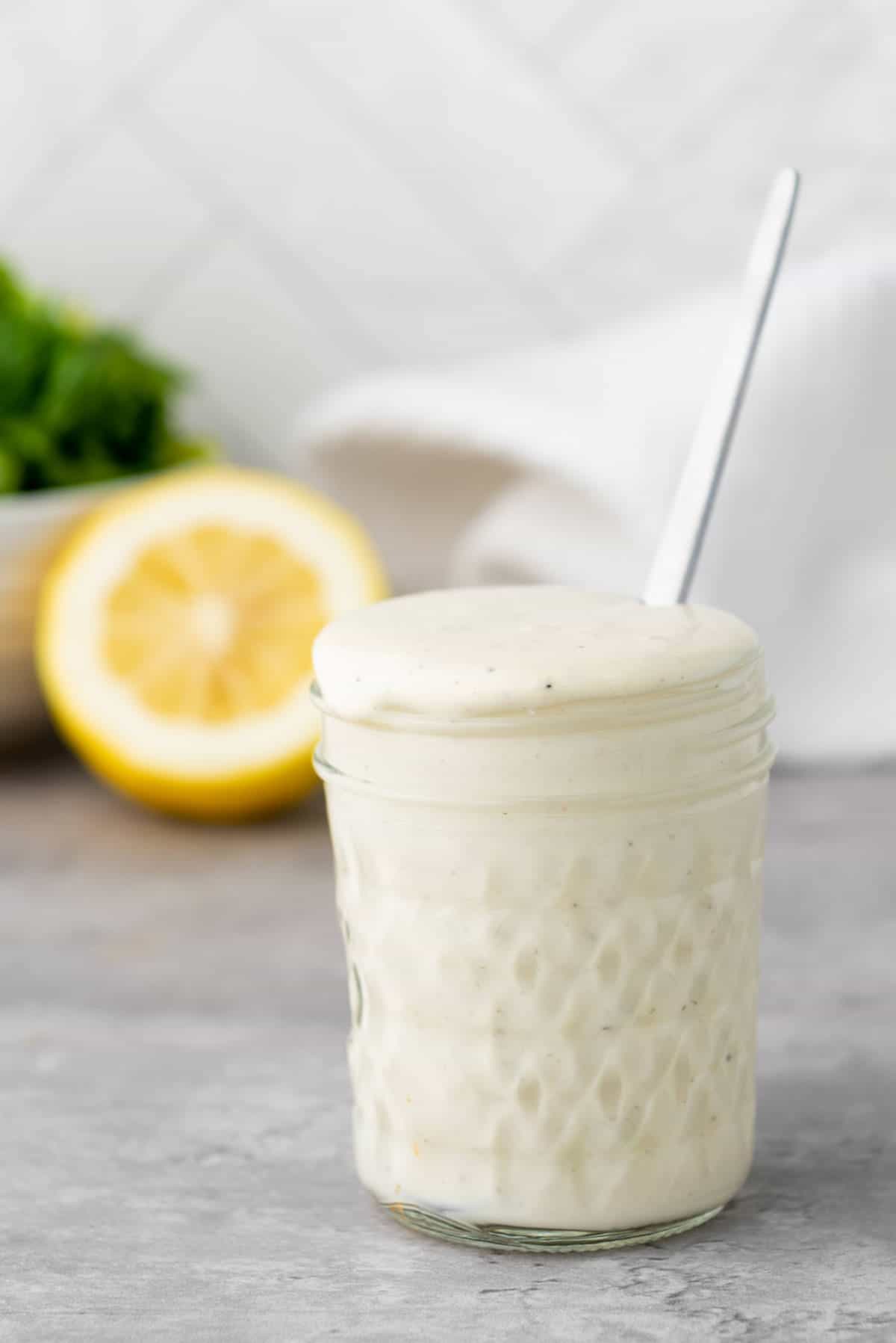 Jar of homemade Caesar salad dressing with a salad in the background.