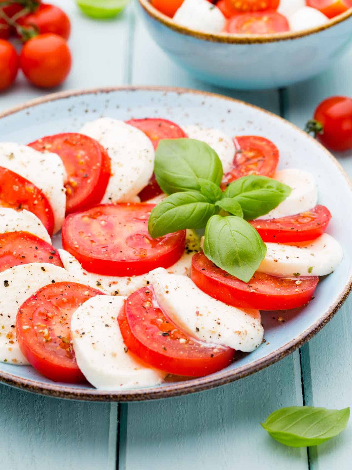 Tomatoes, mozzarella cheese, basil and spices on gray slate stone chalkboard. Italian traditional caprese salad ingredients.