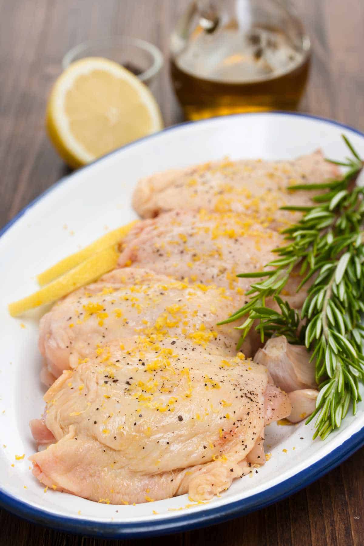 raw chicken thighs with lemon and rosemary on a white plate.