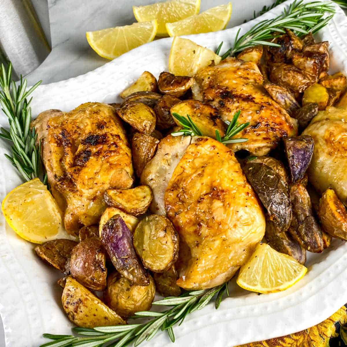 White serving platter filled with air fried chicken thighs with small red potatoes, rosemary, and lemon wedges.