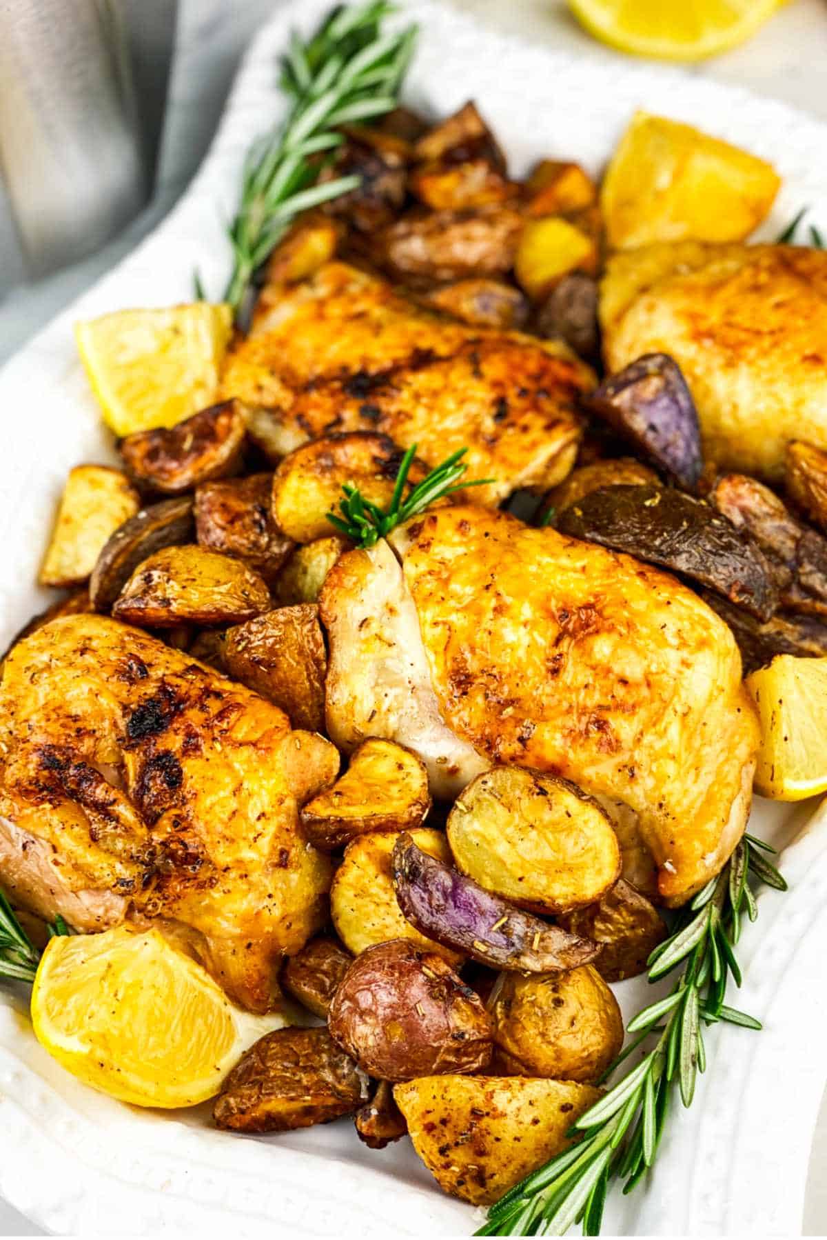 White serving platter filled with air fried chicken thighs with small red potatoes, rosemary, and lemon wedges.