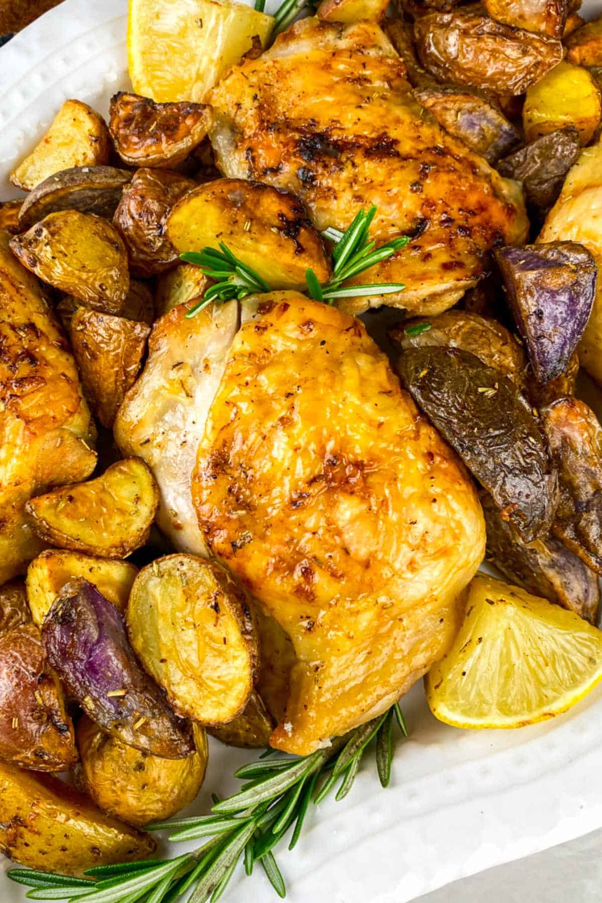 White serving platter filled with air fried chicken thighs with small red potatoes, rosemary, and lemon wedges.