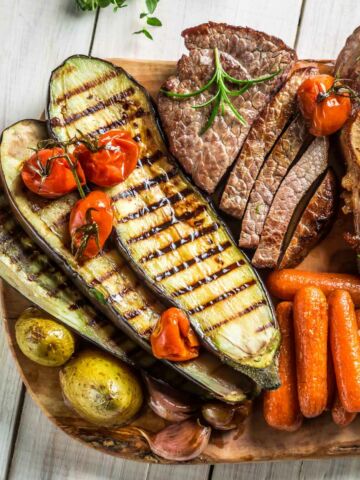 Roasted vegetables and steak with salt on white table.