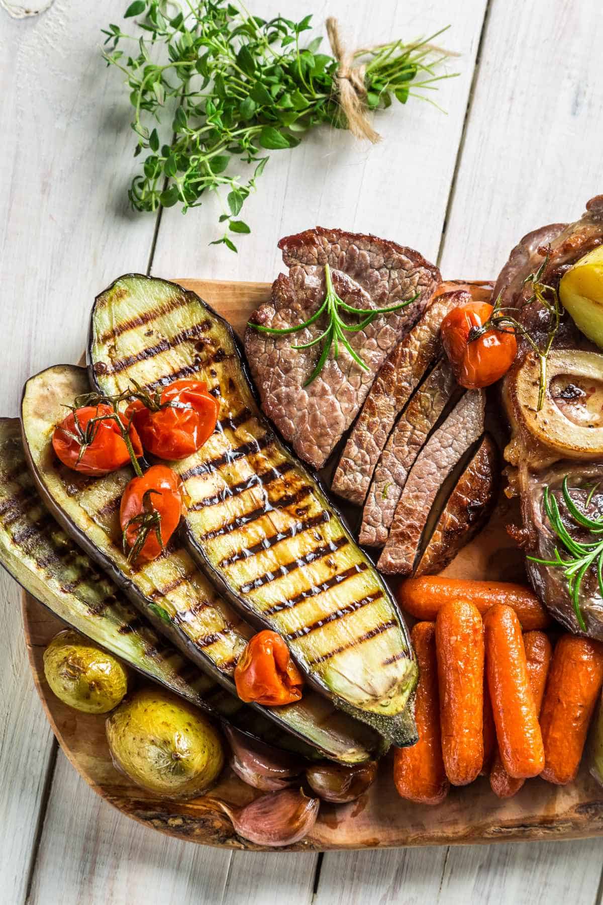 Roasted vegetables and steak with salt on white table.