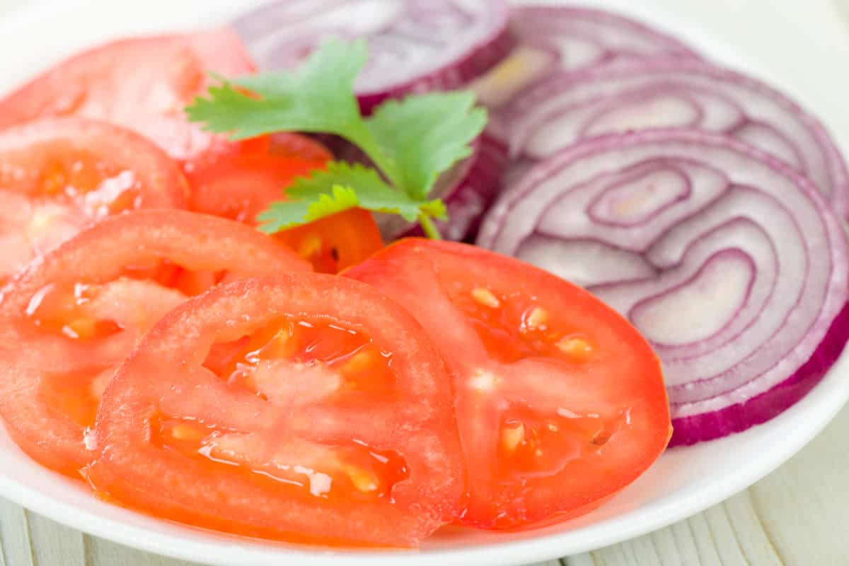 perfectly sliced tomatoes and red onions on a plate.