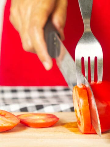 using a fork to help cut a tomato into perfect slices.