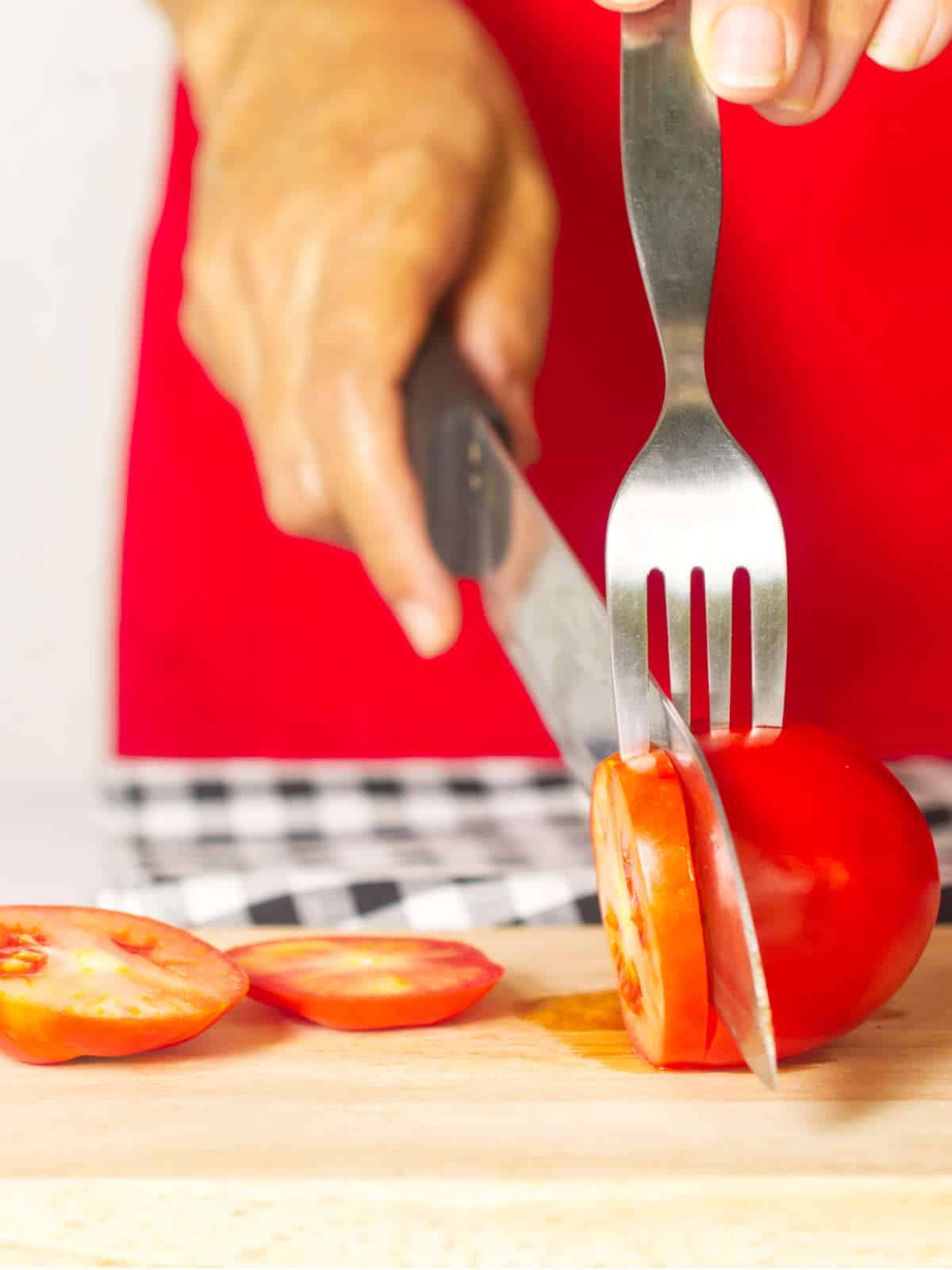 using a fork to help cut a tomato into perfect slices.