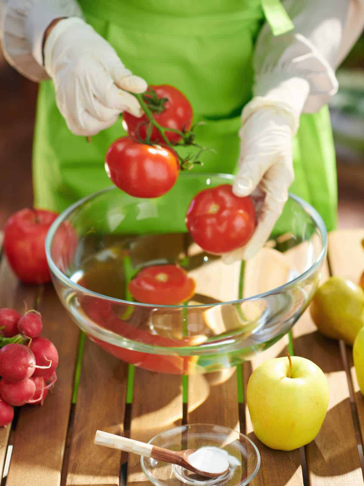 Closeup on female in green apron removes pesticides by soaking vegetables and fruits in water with baking soda in modern kitchen.