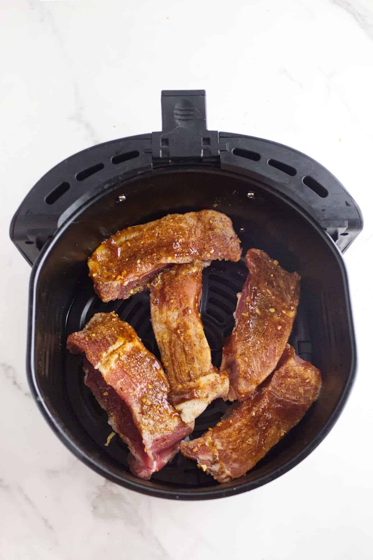 raw seasoned country pork ribs in an air fryer basket.