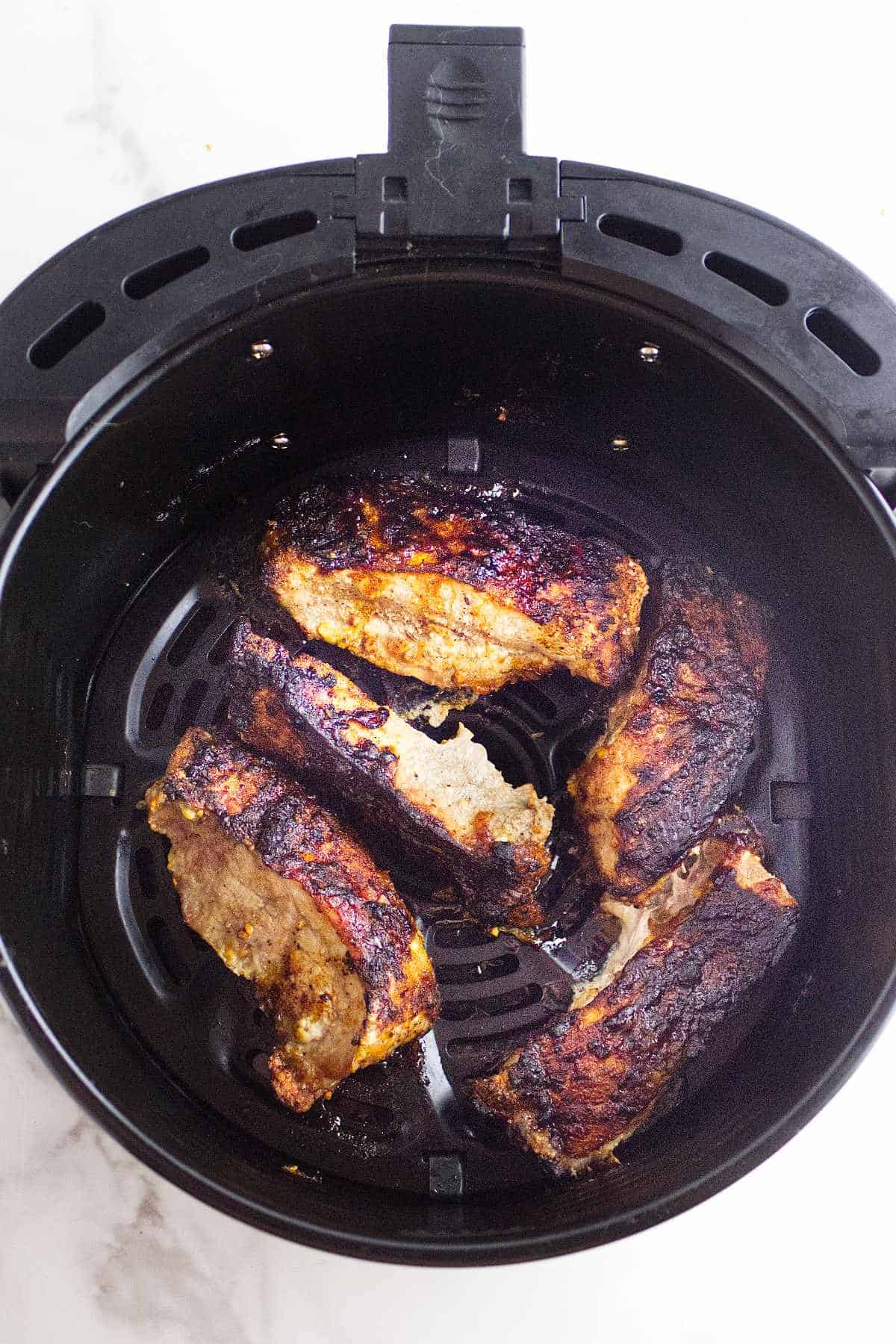 cooked ribs in an air fryer basket.